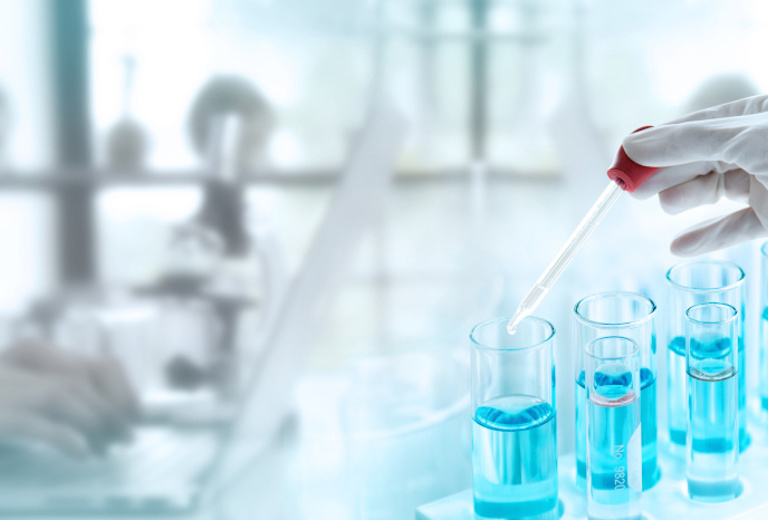 Laborpersonal arbeitet mit Pipette an Tisch mit Laborgeräten