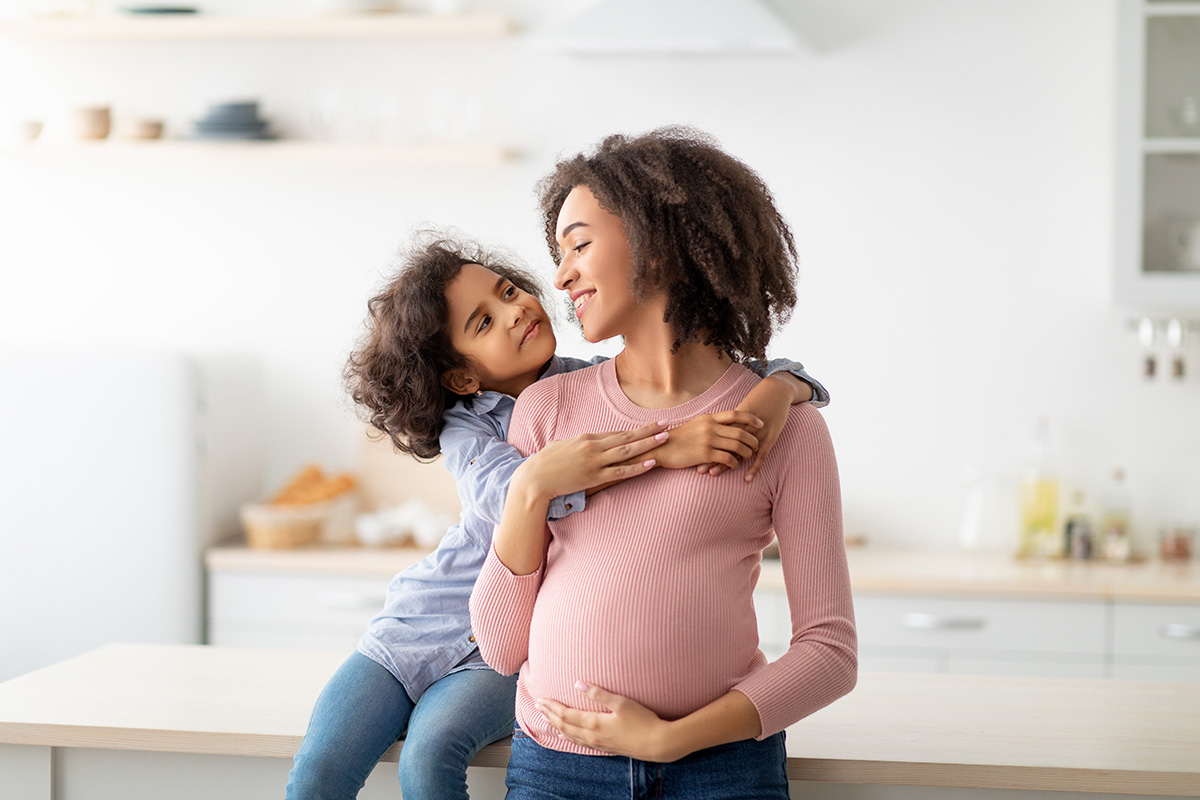 Schwangere Mutter wird von Kind in den Arm genommen
